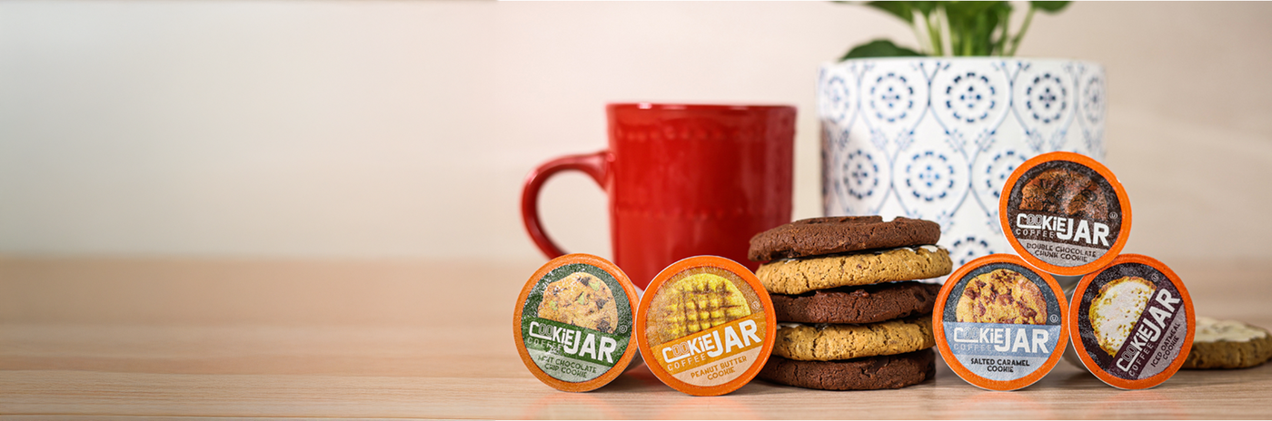 An image of a red coffee mug behind cookie jar coffee pods and a stack of cookies. 